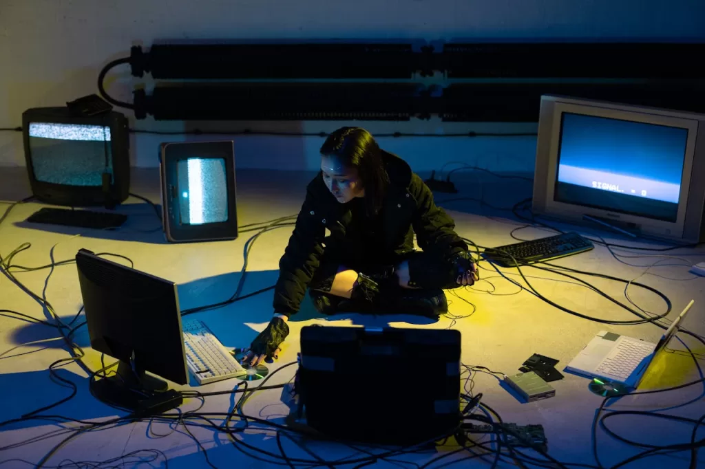 Person surrounded by multiple screens and cables in a dark room, illustrating digital overwhelm and constant connectivity in 2026